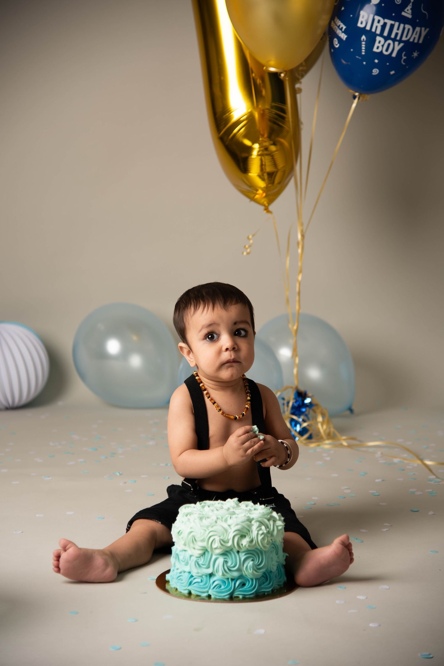 Birthday celebration setup with blue and gold balloons and a turquoise ombre smash cake.