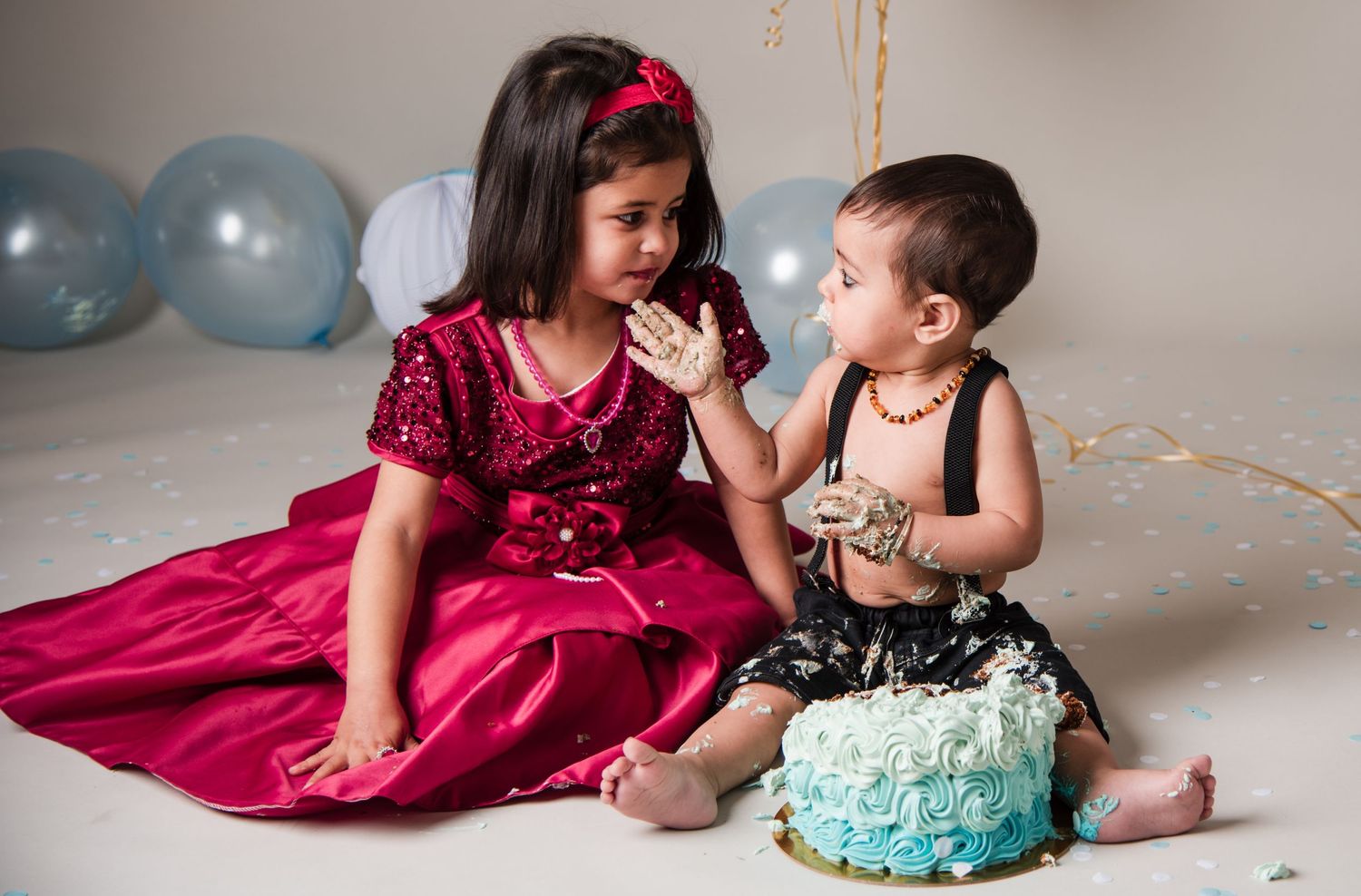 Children sitting together with blue birthday cake and balloons in celebration setting.