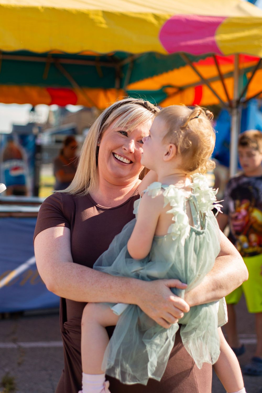 A joyful moment shared between a woman in brown and a small child in a mint green dress at an outdoor event.