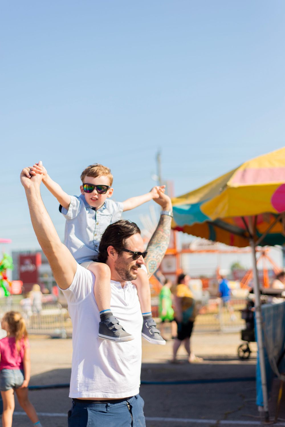 Fun summer day at the carnival with people enjoying activities under colorful umbrellas and bright blue sky.