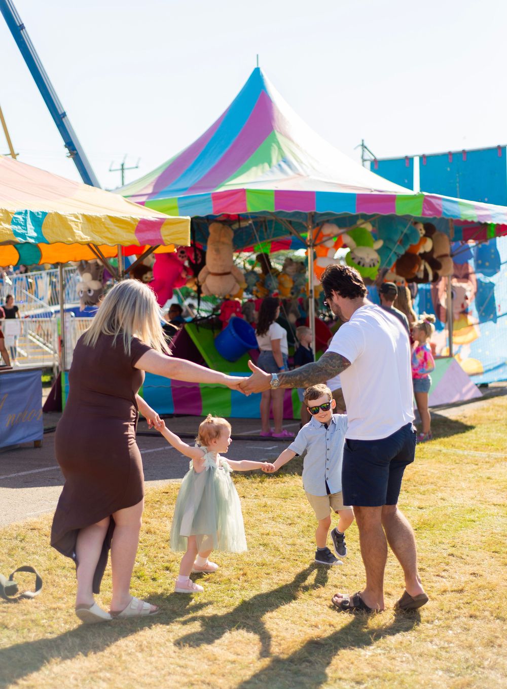 People dancing together at a colorful carnival fairground with tents and festive decorations in the background.