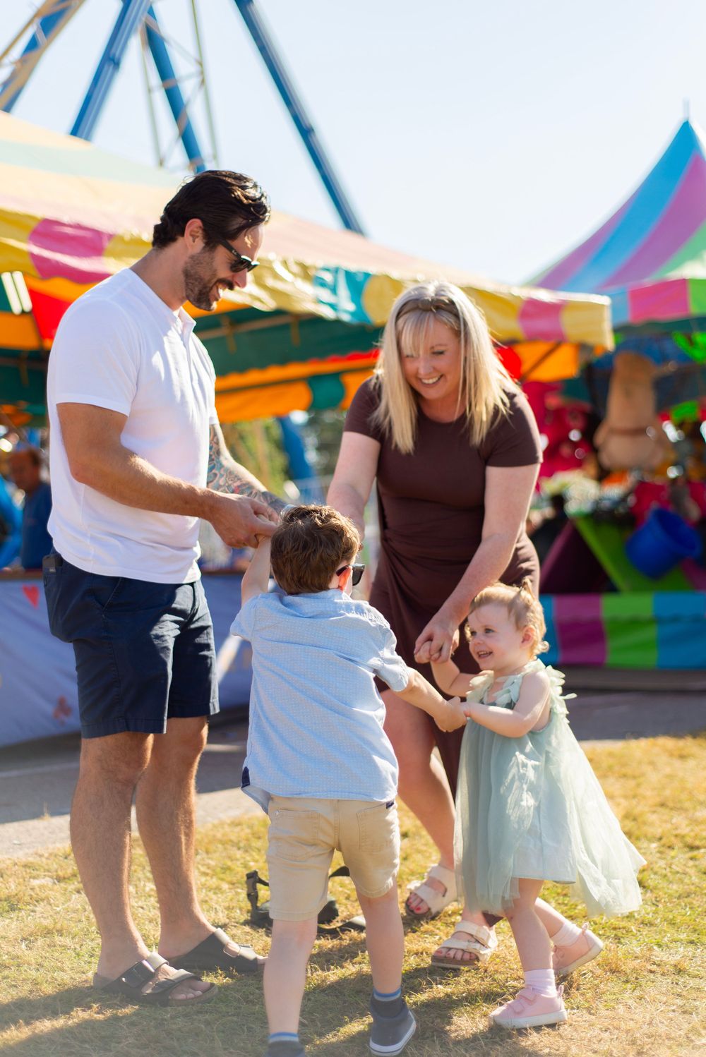 Family enjoying a fun day at a carnival with colorful tents and rides in the background.