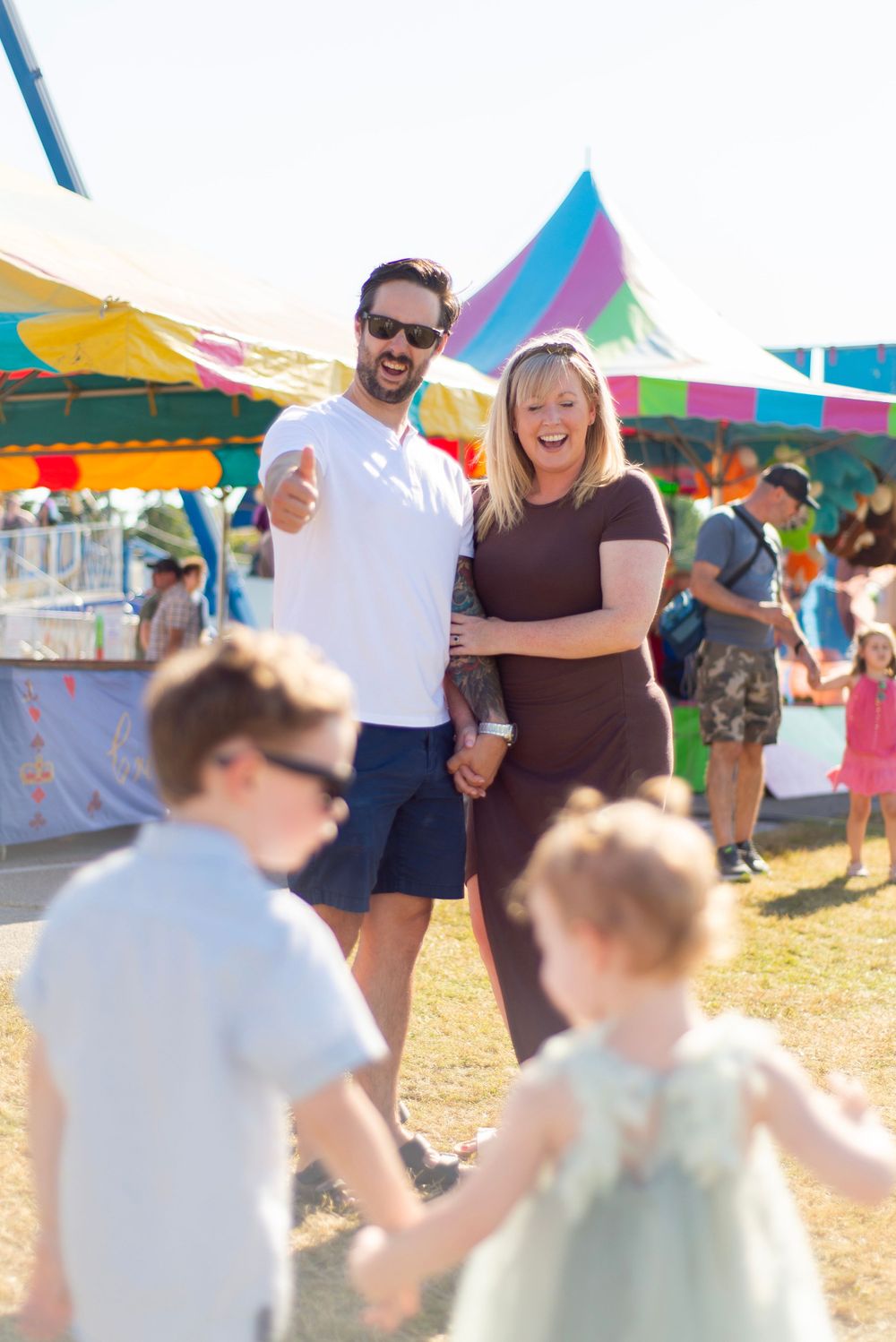 People enjoying a sunny day at an outdoor festival with colorful tents and banners in the background.