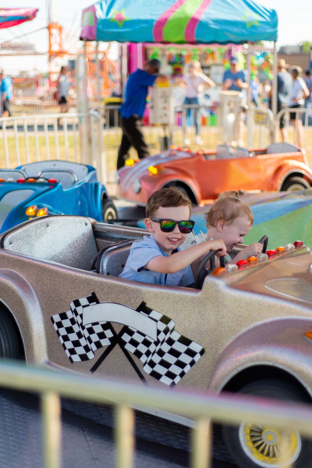 Children enjoying a carnival ride in colorful vintage-style toy cars decorated with racing flags.