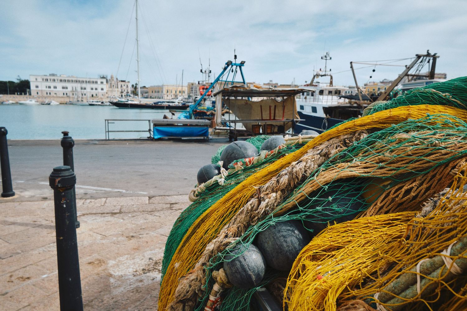 Colorful fishing nets and equipment on a harbor dock with boats in the background on a sunny day.