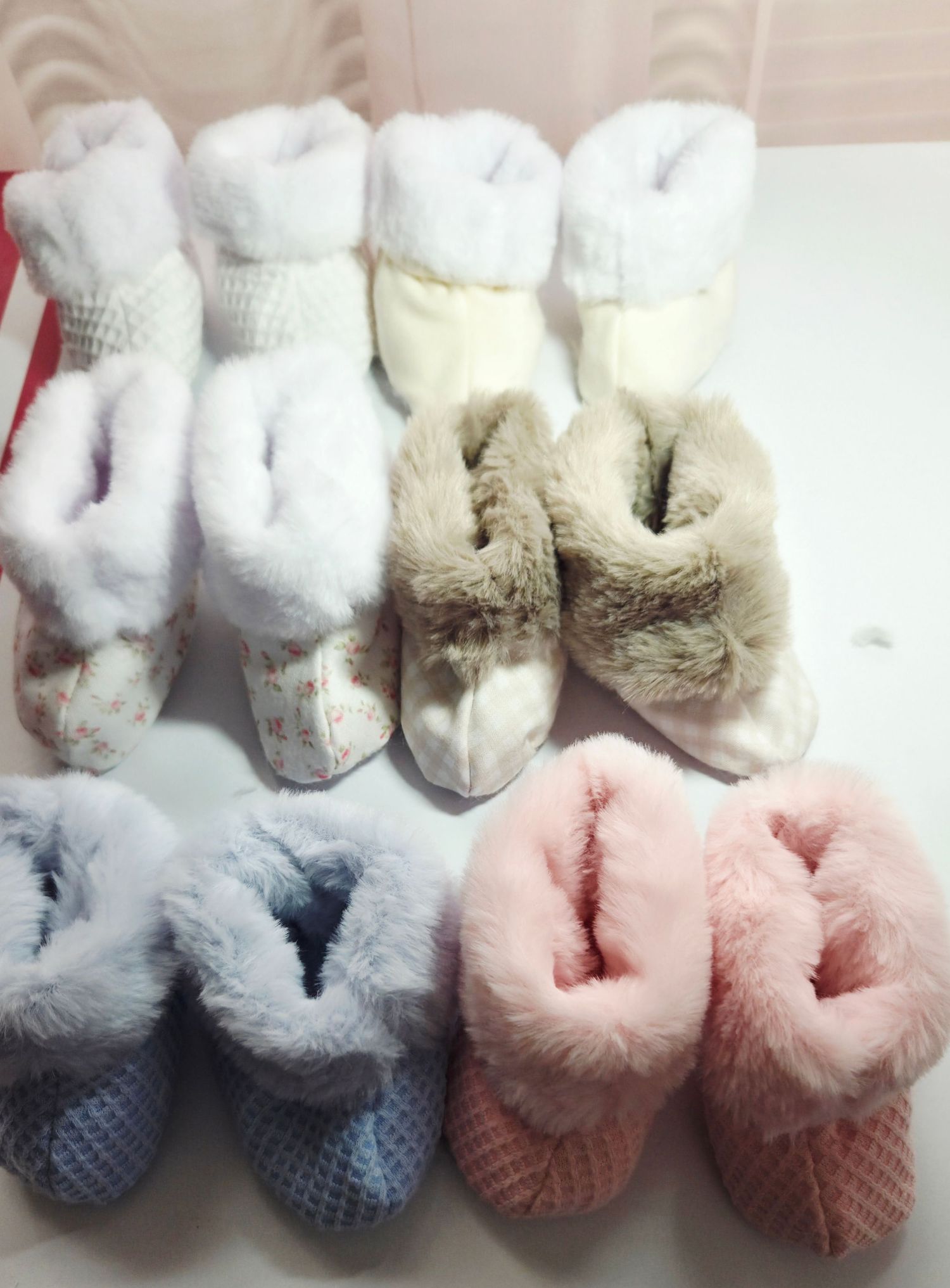 Collection of cozy baby booties in white, beige, blue, and pink with fluffy faux fur trim displayed in pairs.