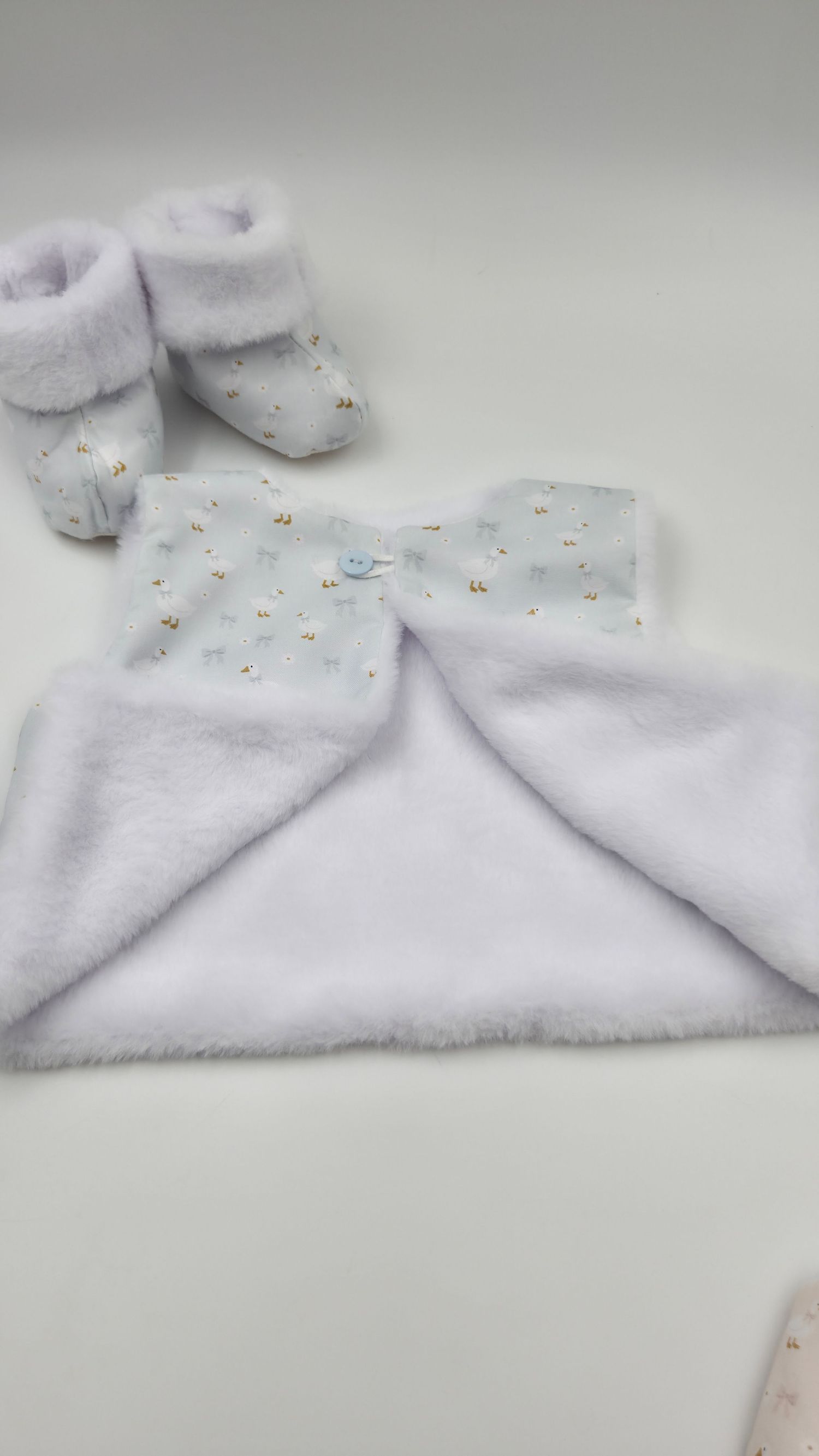 White fluffy baby blanket with blue floral print trim and matching soft booties set on white background.