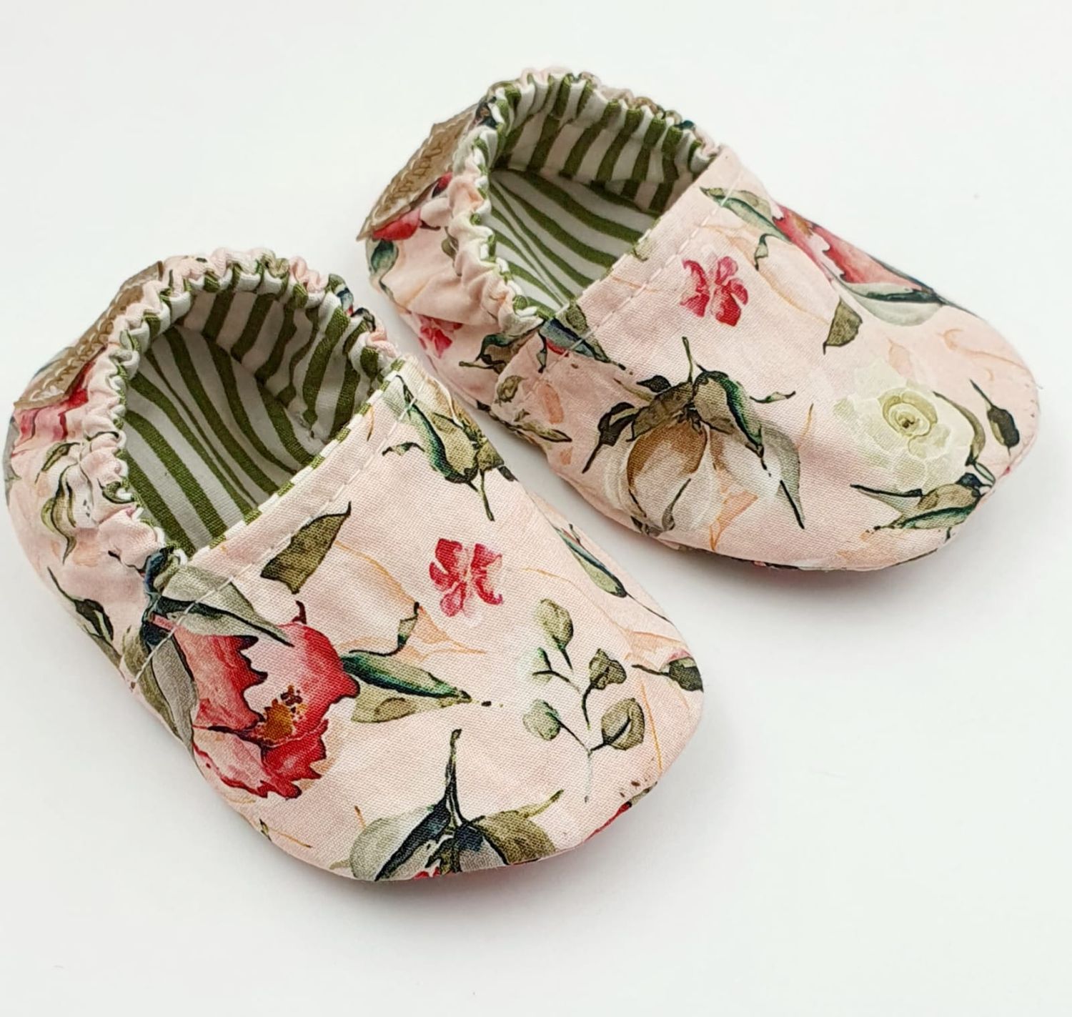 Pink floral baby shoes with green striped interior lining viewed from different angles.