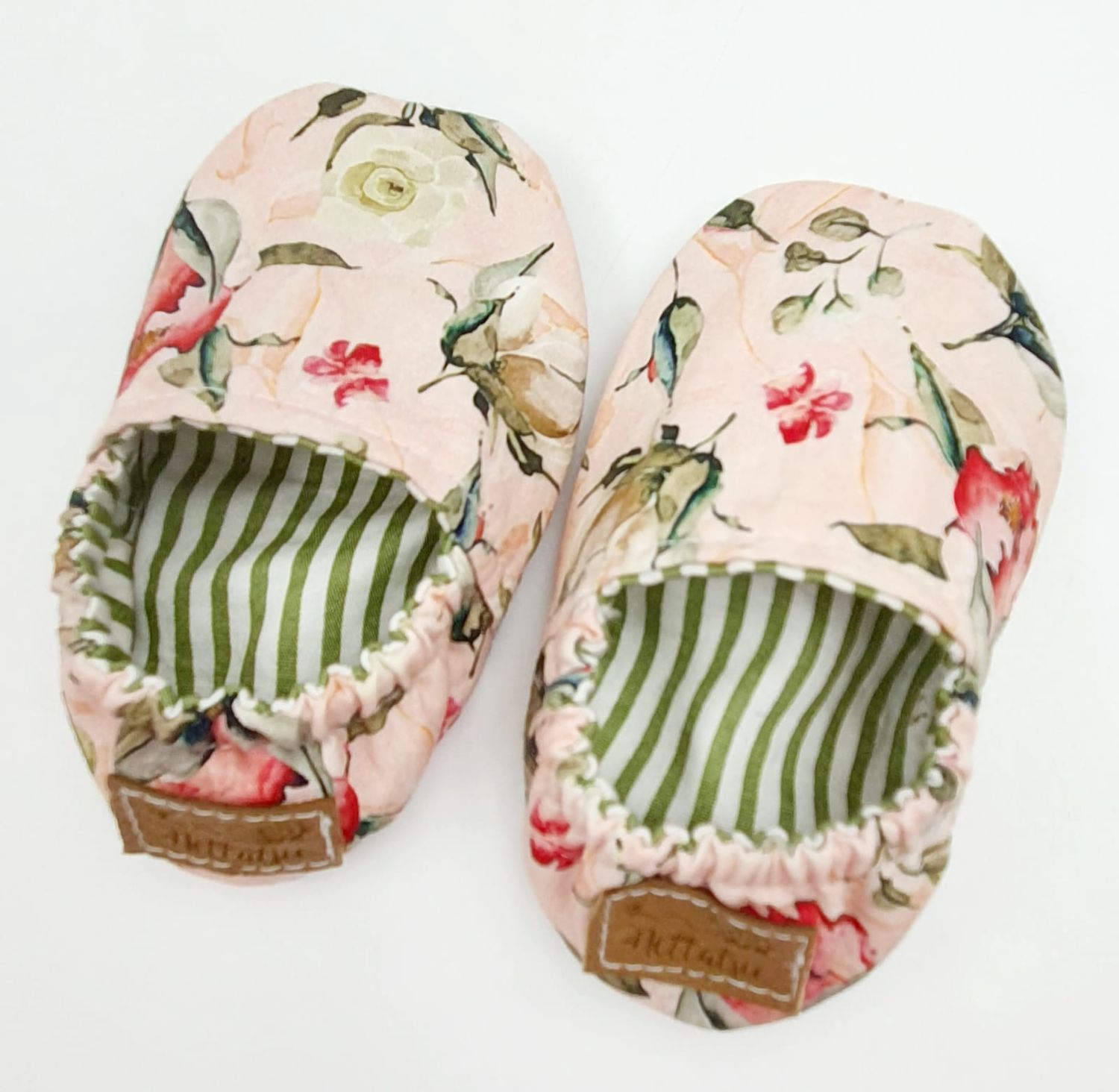 Floral print baby shoes with green striped lining shown from above.
