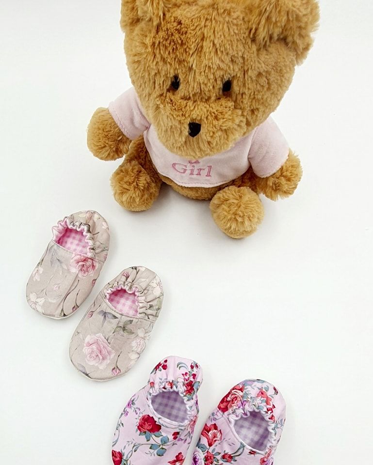 Tan plush bear with pink floral baby shoes and clothing accessories.