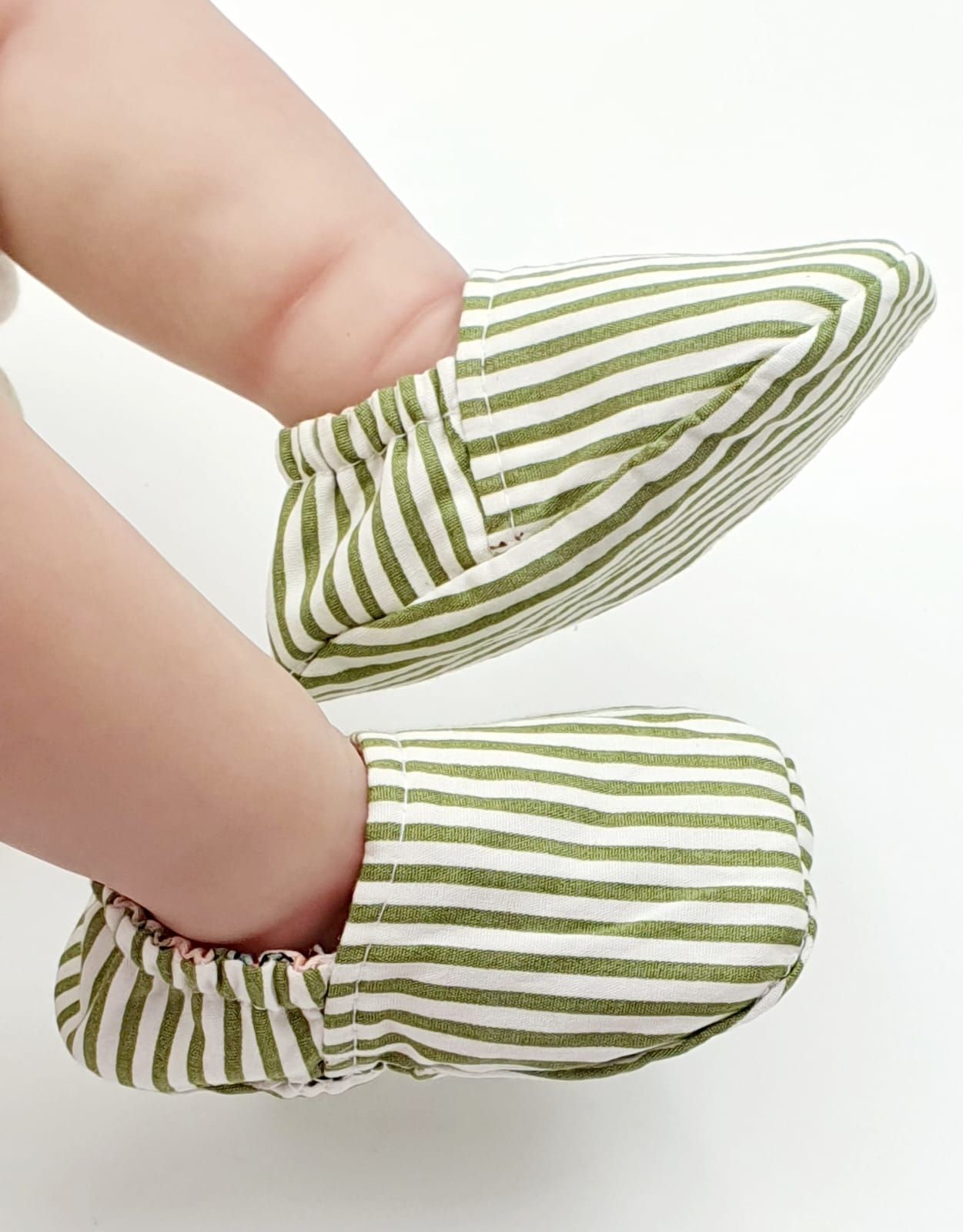 Green and white striped baby shoes being worn on small feet.