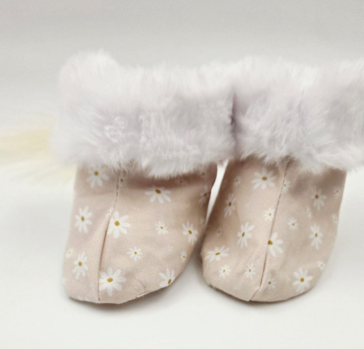 Pink floral baby booties with white faux fur trim, featuring daisy pattern, perfect for newborn girls.
