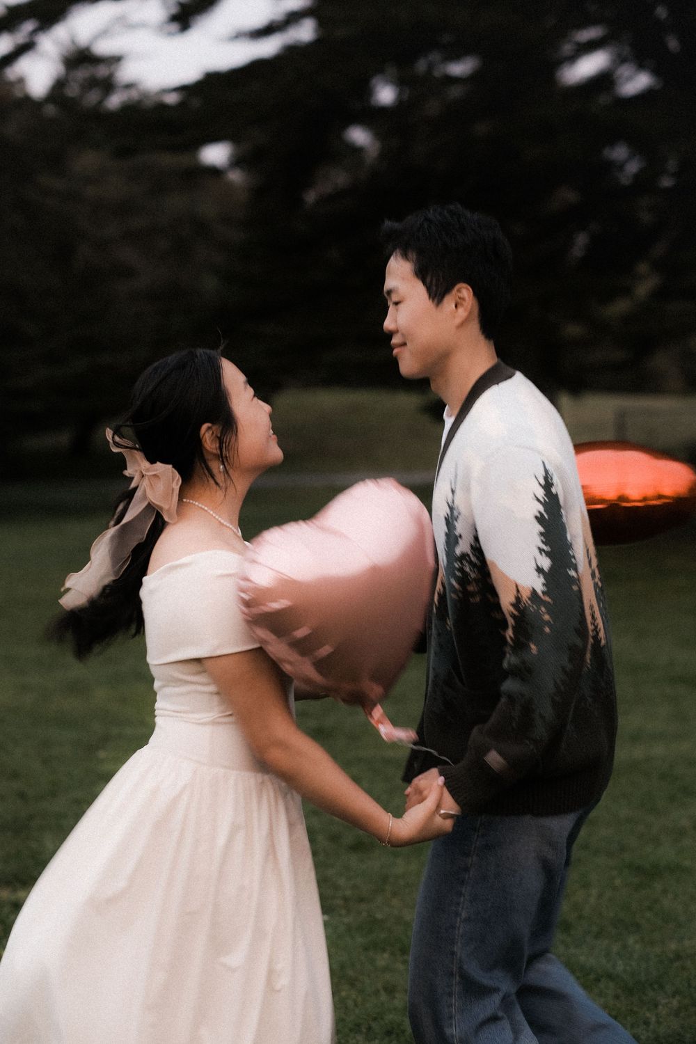A romantic couple in a park holds hands while a heart-shaped balloon floats between them.