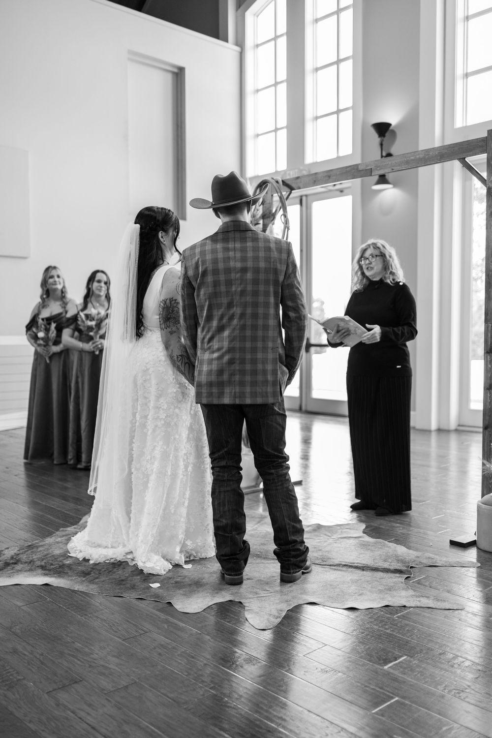 A black and white wedding ceremony in a bright indoor venue with tall windows and hardwood floors.