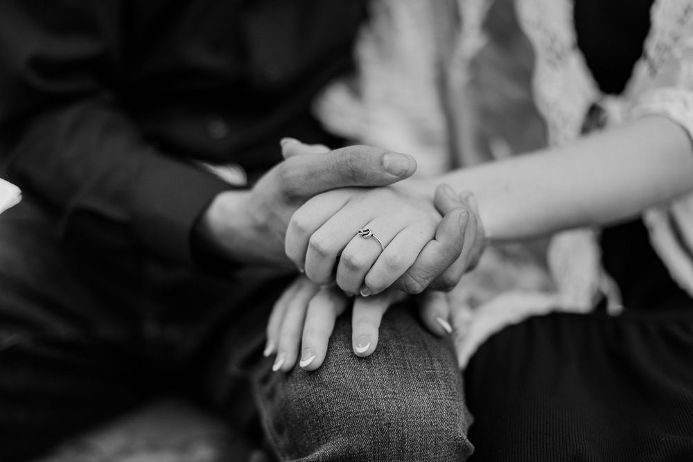 Black and white photo of couple holding hands showing engagement ring.