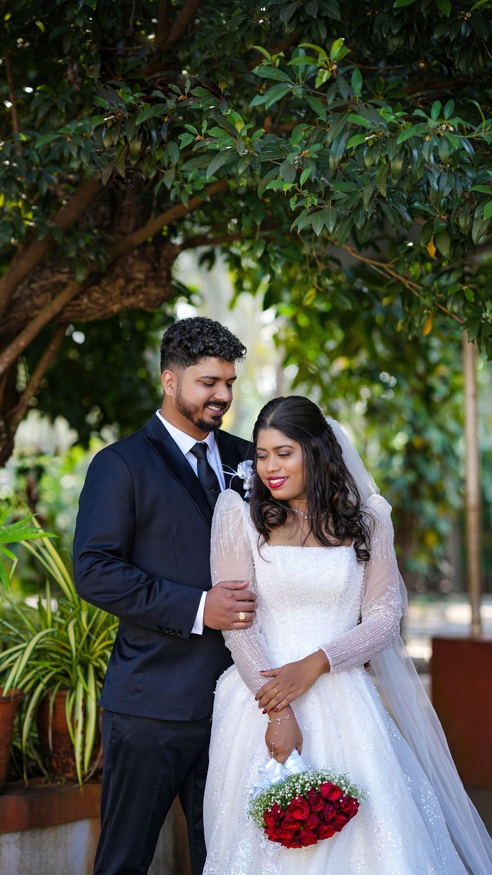 Bride and groom standing together outdoors beneath a tree