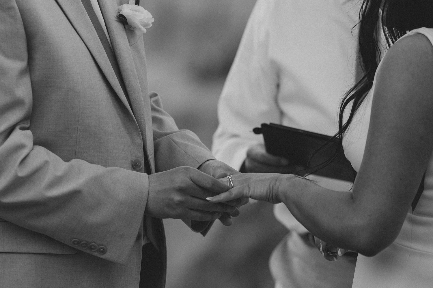 A close-up black and white shot of hands exchanging rings during a wedding ceremony.