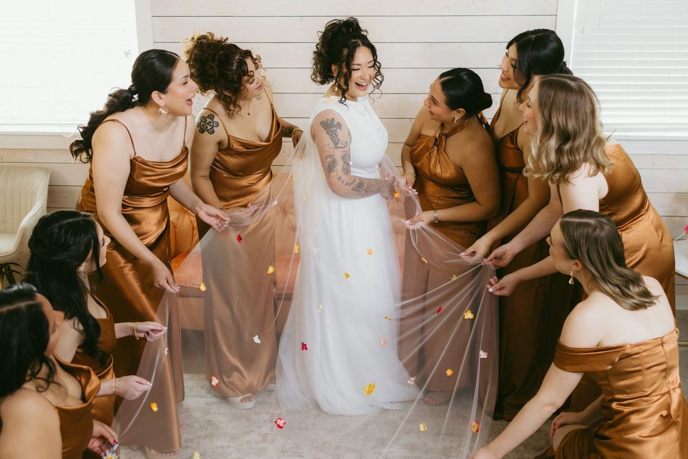 A group of women in brown dresses gather together during a wedding preparation moment.
