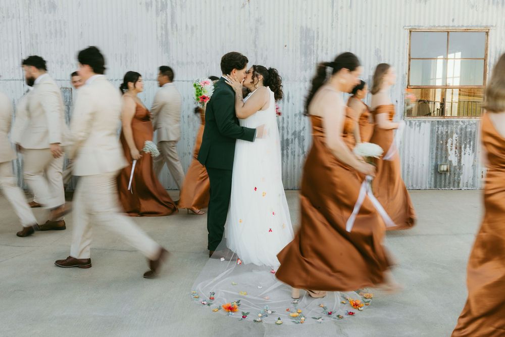 Wedding party in motion with bridesmaids in rust-colored dresses and groomsmen in light suits walking past a couple dancing.
