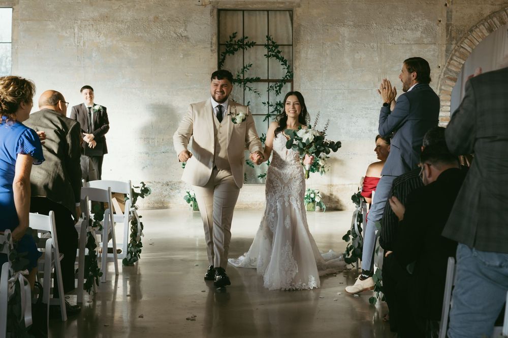 Wedding guests gather in an industrial venue space with white walls and exposed beams during a celebration.