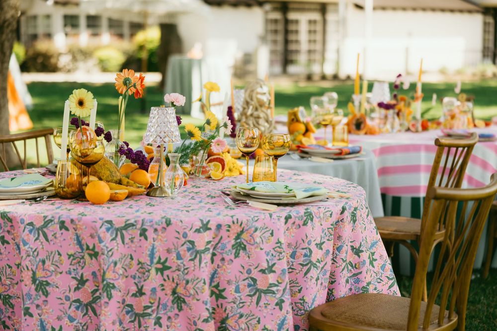 Elegant garden party table settings with pink floral tablecloths and yellow pumpkin centerpieces create a festive autumn atmosphere.