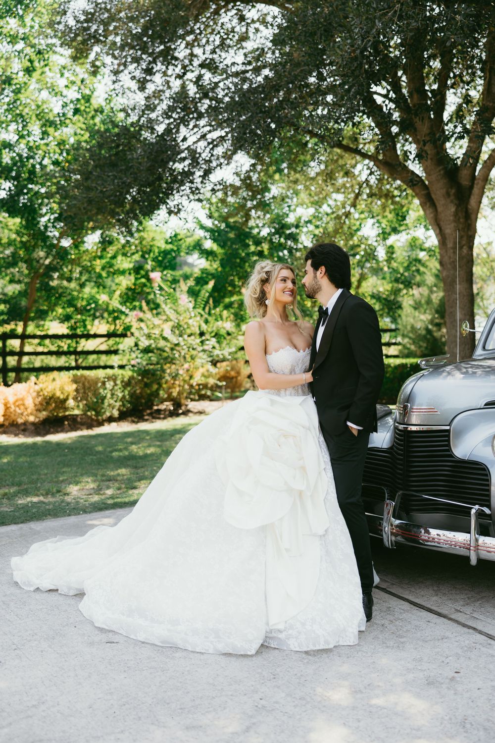 A romantic wedding photo series showing a couple posing with a classic vintage car in a sunlit outdoor setting.