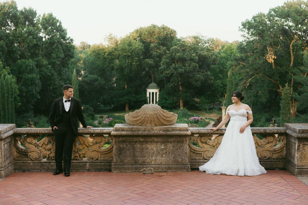 Bride and groom share intimate moments during their wedding photoshoot in a scenic garden with stone architecture.