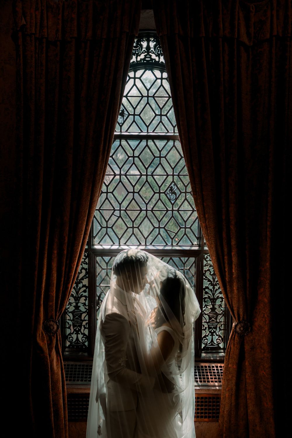 Silhouette through ornate stained glass window with flowing veil and dramatic lighting.