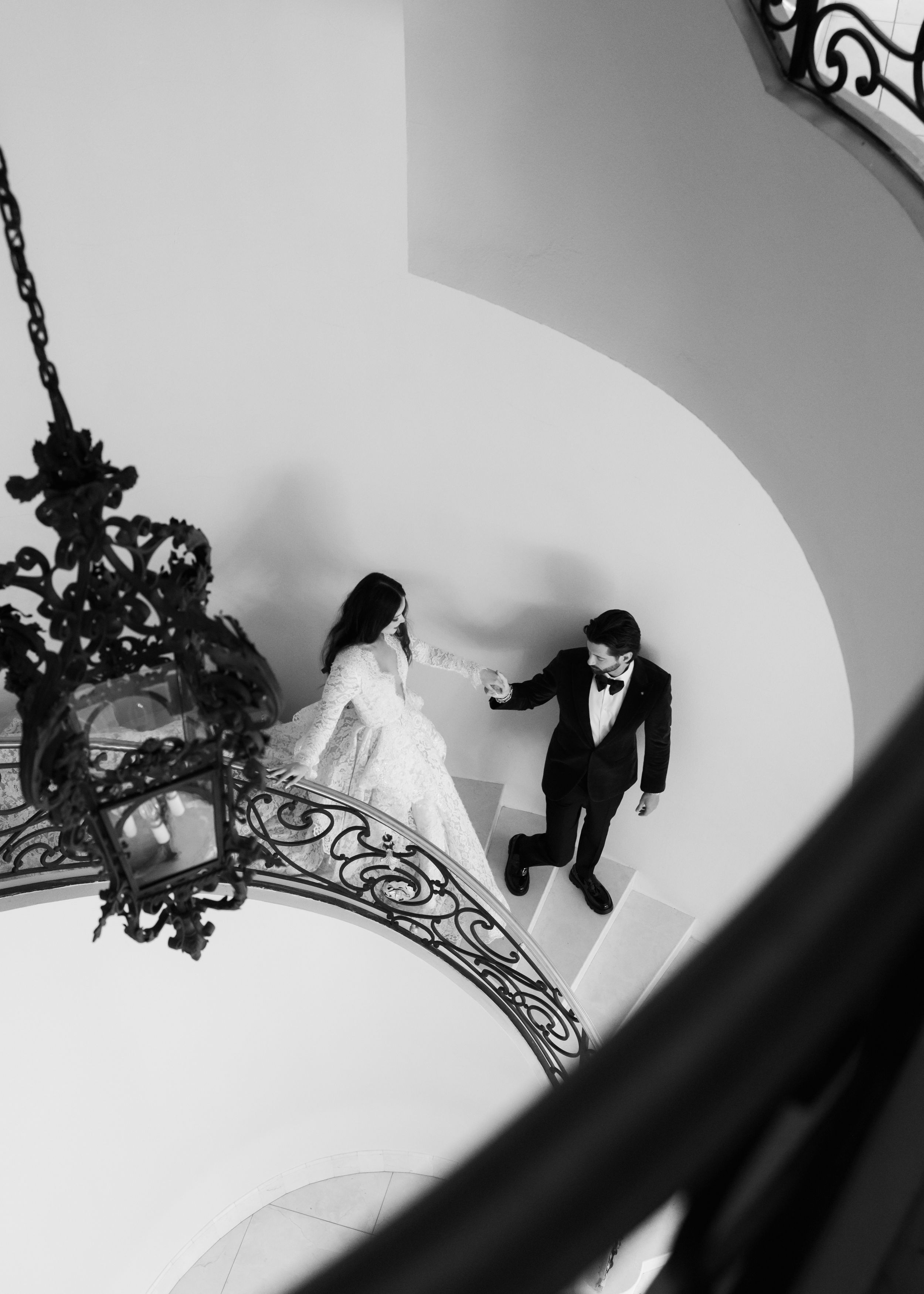 Couple poses on garden staircase surrounded by lush greenery and cypress trees.