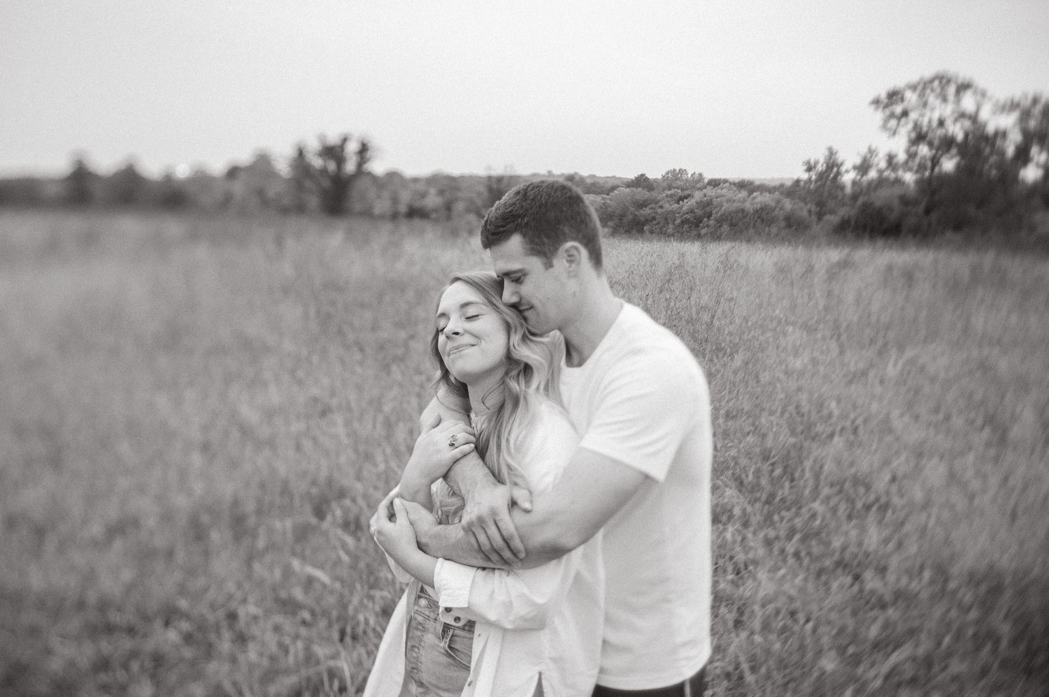 husband giving his wife a loving hug standing in an open field at shawnee mission park in shawnee kansas
