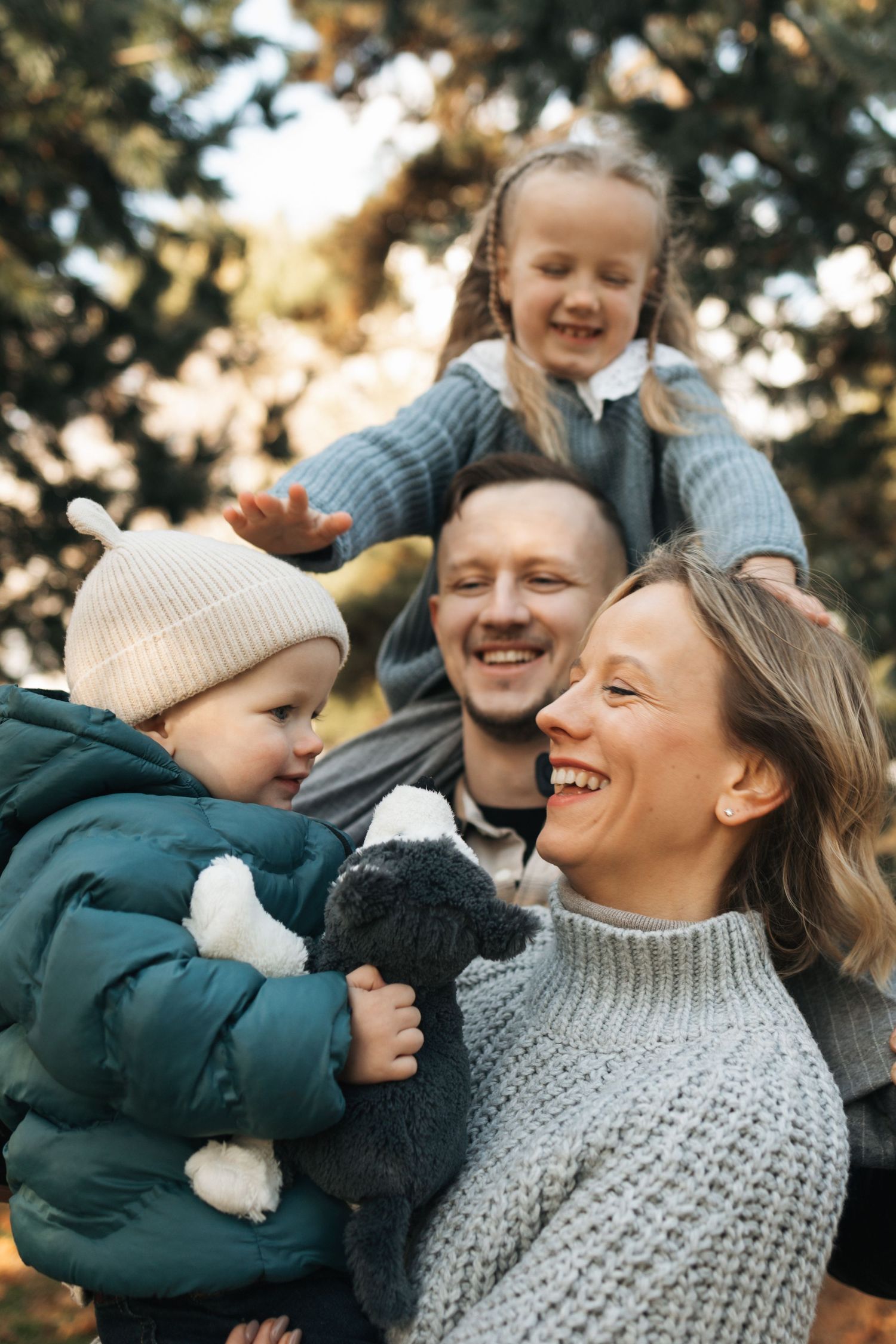 Happy family with two young children smiling outdoors among evergreen trees in autumn.