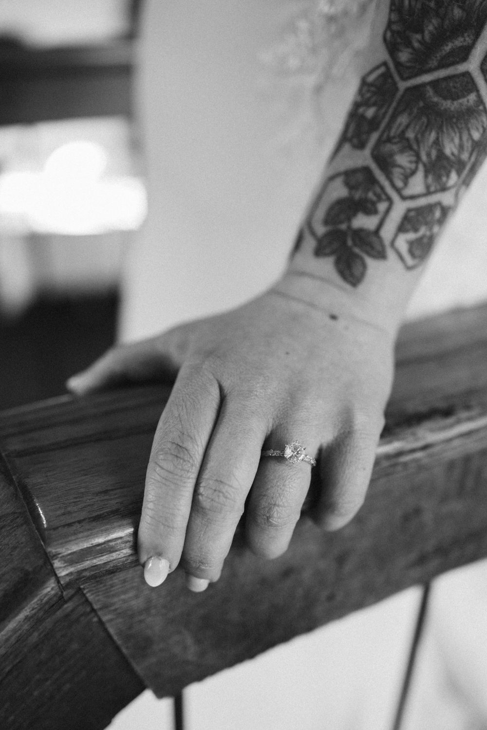 Black and white photo of a hand with tattoo resting on wood, wearing an engagement ring on ring finger near hackettstown nj..