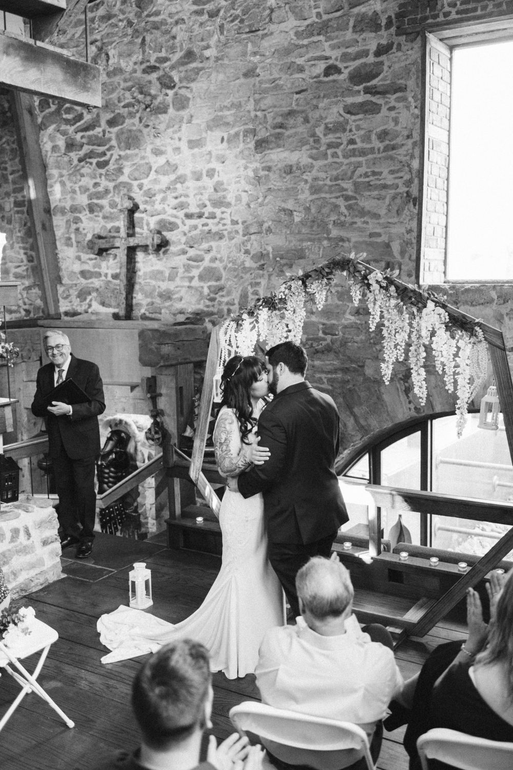 A black and white wedding ceremony in a rustic stone wall venue with flowing floral decorations and a cross on display near hackettstown nj.