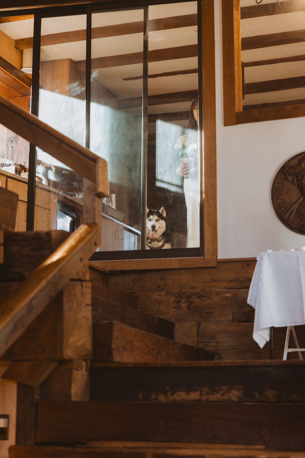 Husky dog peeks through glass panel on wooden staircase in rustic interior with exposed beams near hackettstown nj.