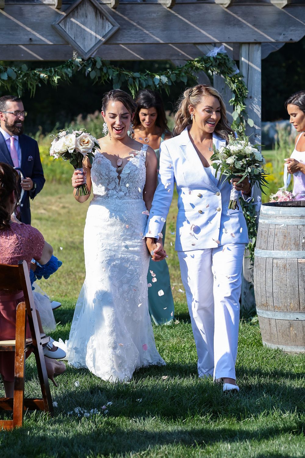 Outdoor wedding ceremony with couples in white attire amid rustic garden decor.