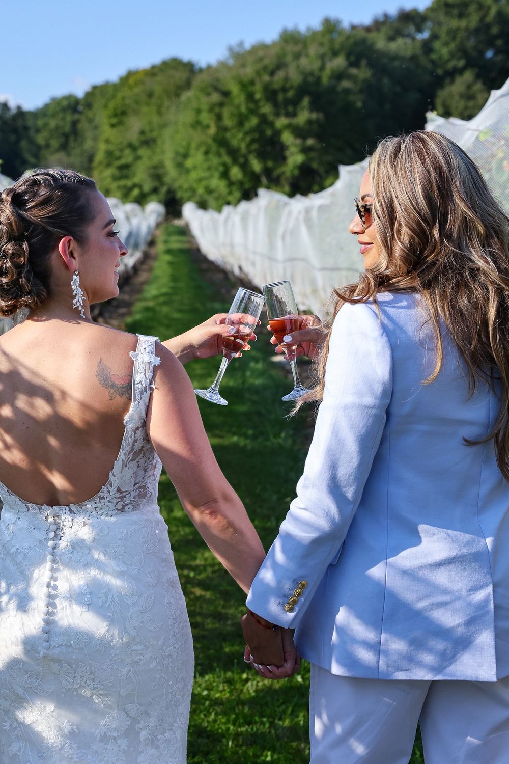A group in white attire celebrates outdoors with drinks in hand against a lush green backdrop.