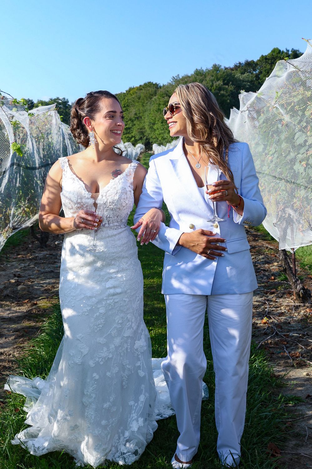 Wedding party members in white outfits laugh and socialize on a sunny outdoor terrace.