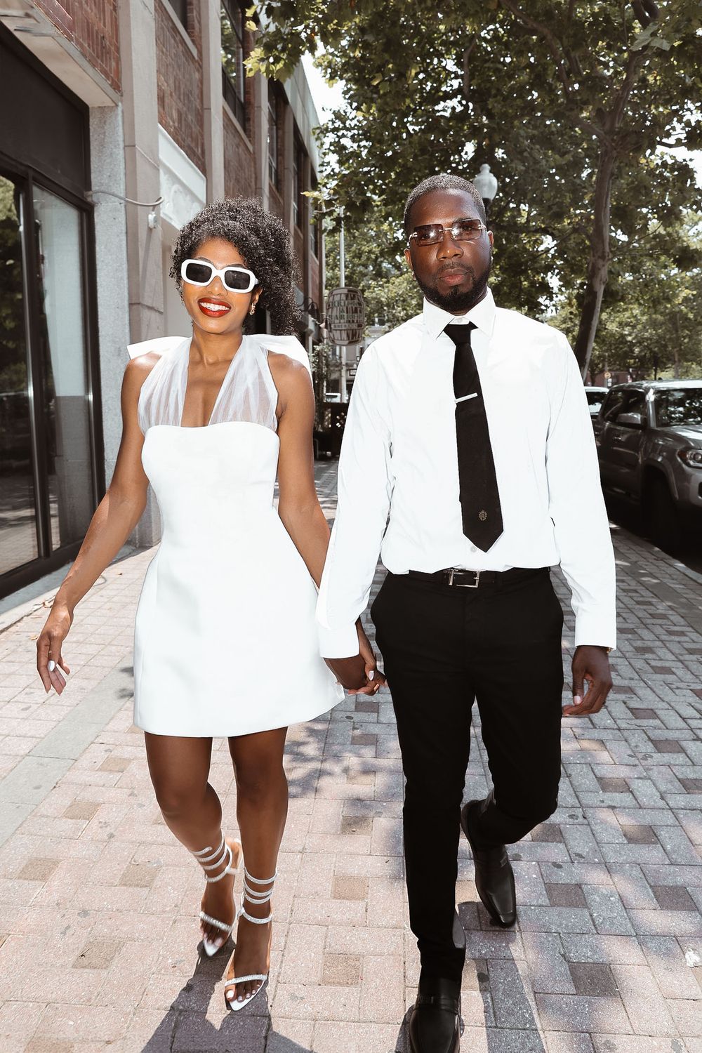 A stylish couple in black and white outfits walk together on a city sidewalk.