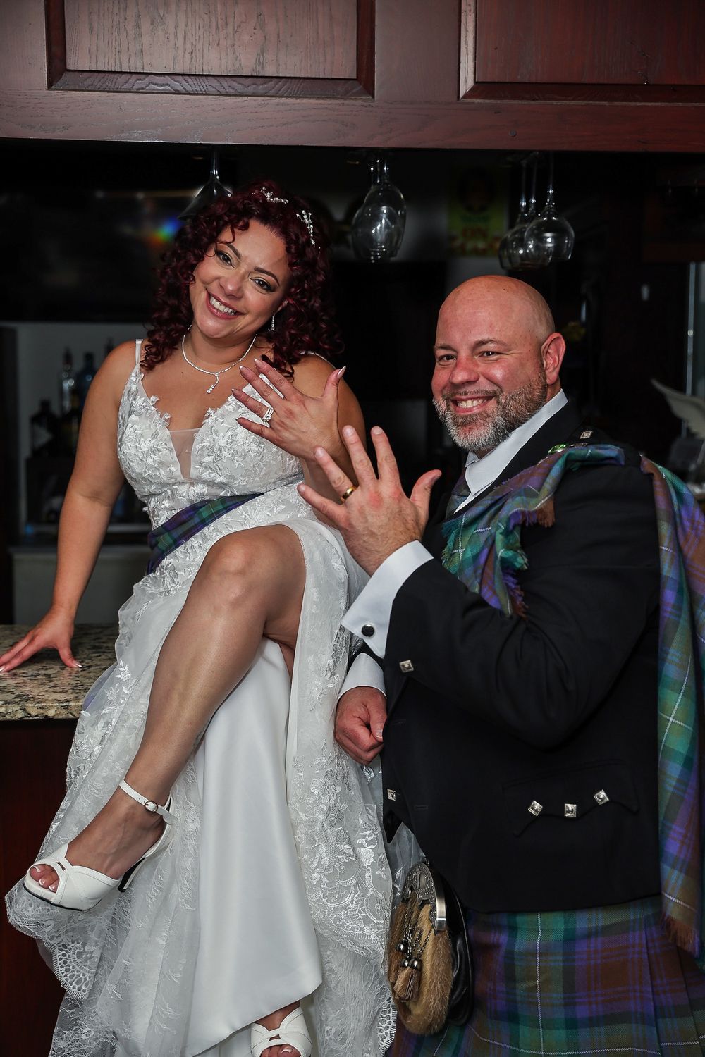 Wedding couple celebrating with bride showing off her shoe while groom wears traditional Scottish attire.