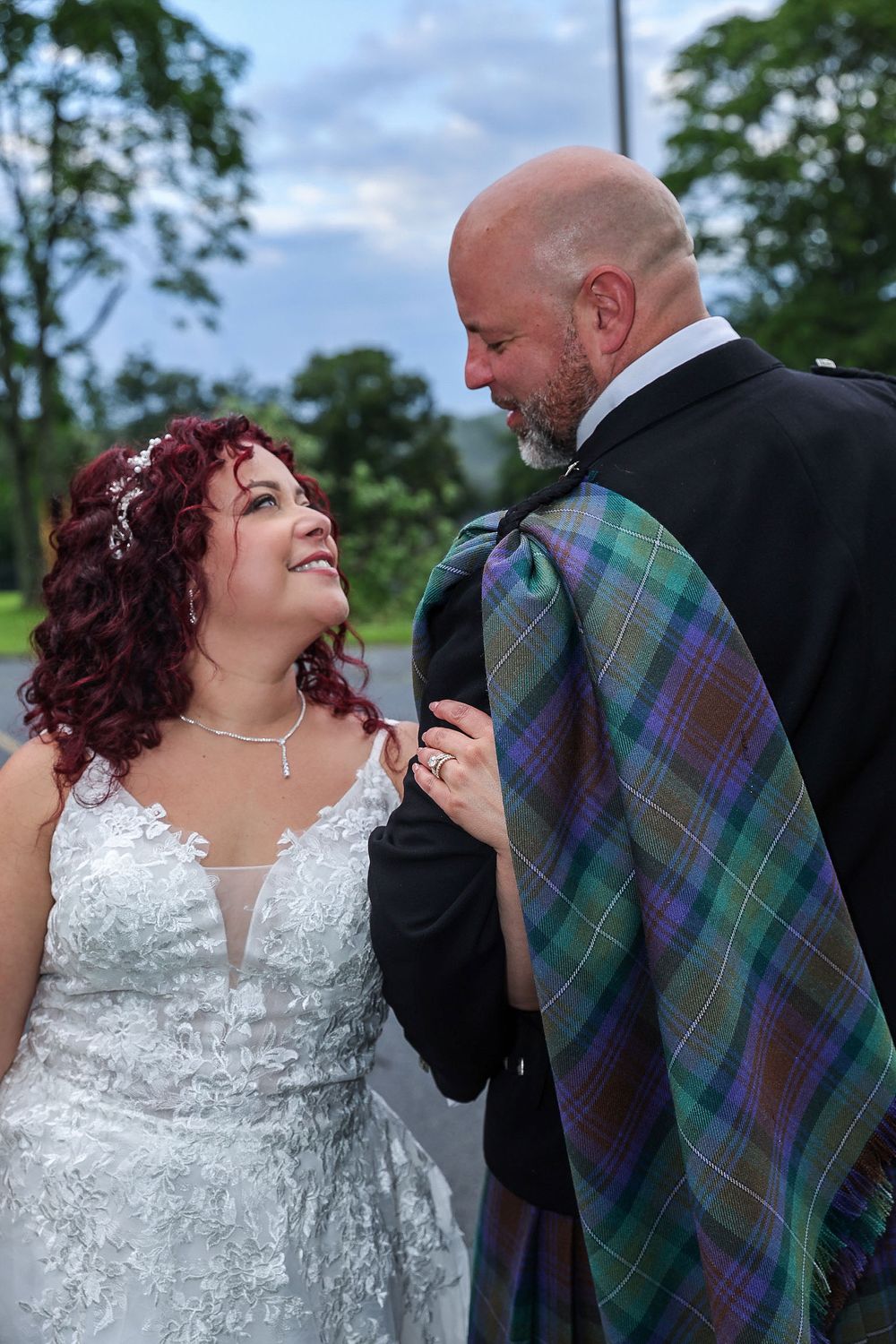 Candid wedding moment with bride in lace gown and groom wearing traditional Scottish formal wear.