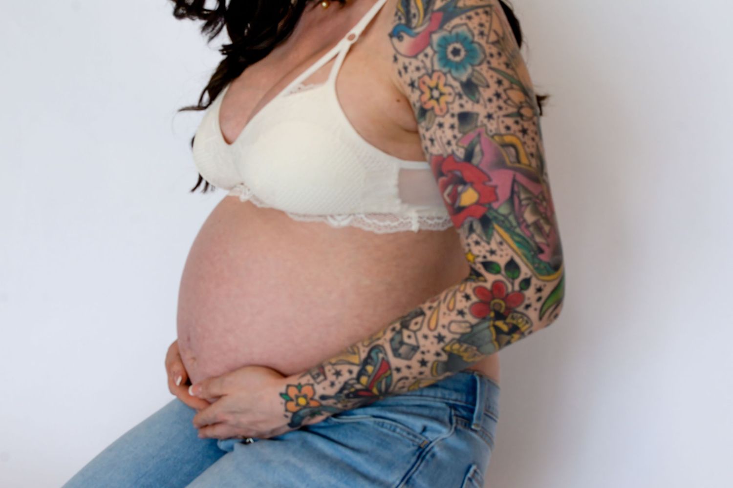 Side view of pregnant person showing decorated belly with artistic tattoo design.