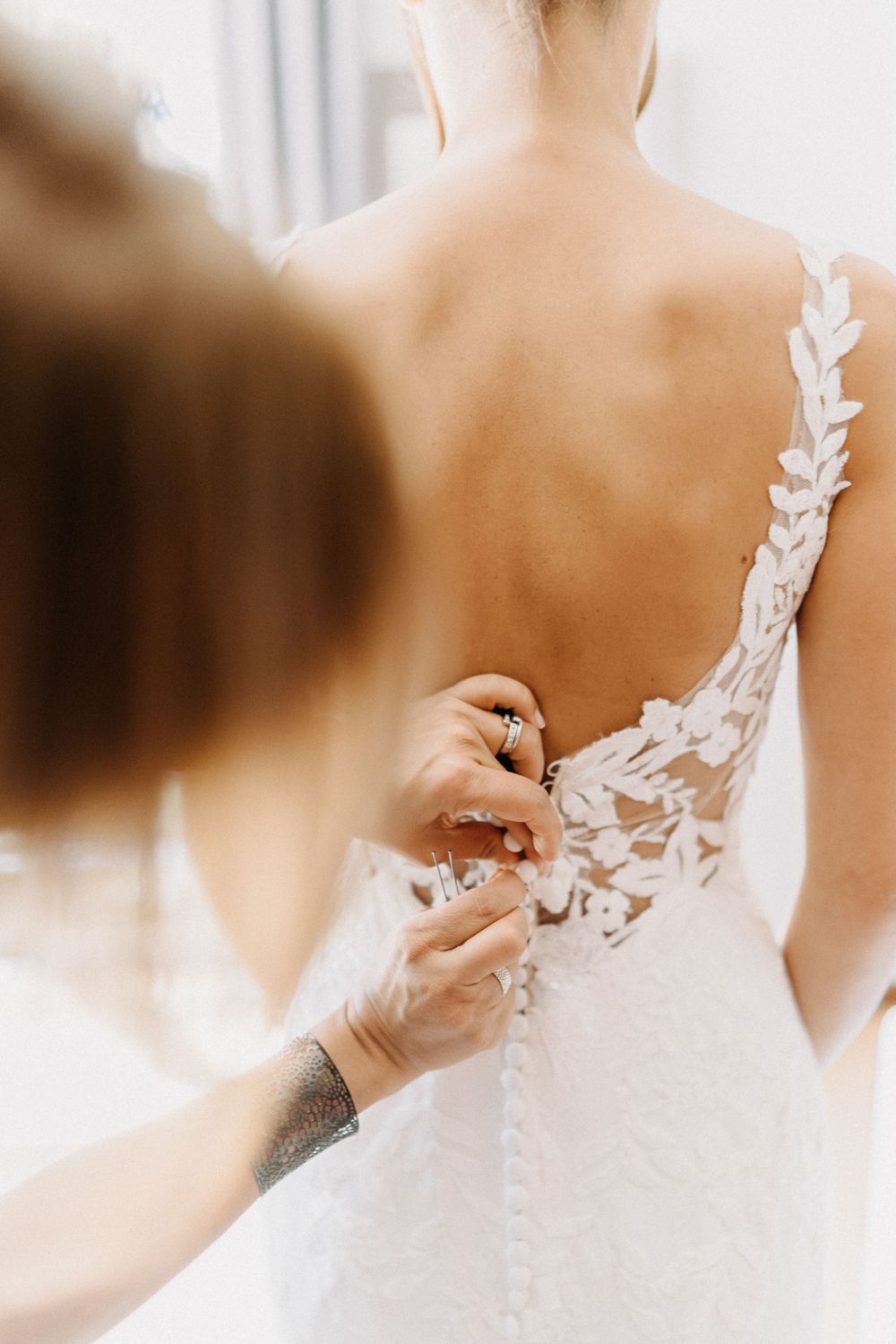 Close-up of delicate lace detail being fastened on back of white wedding dress.