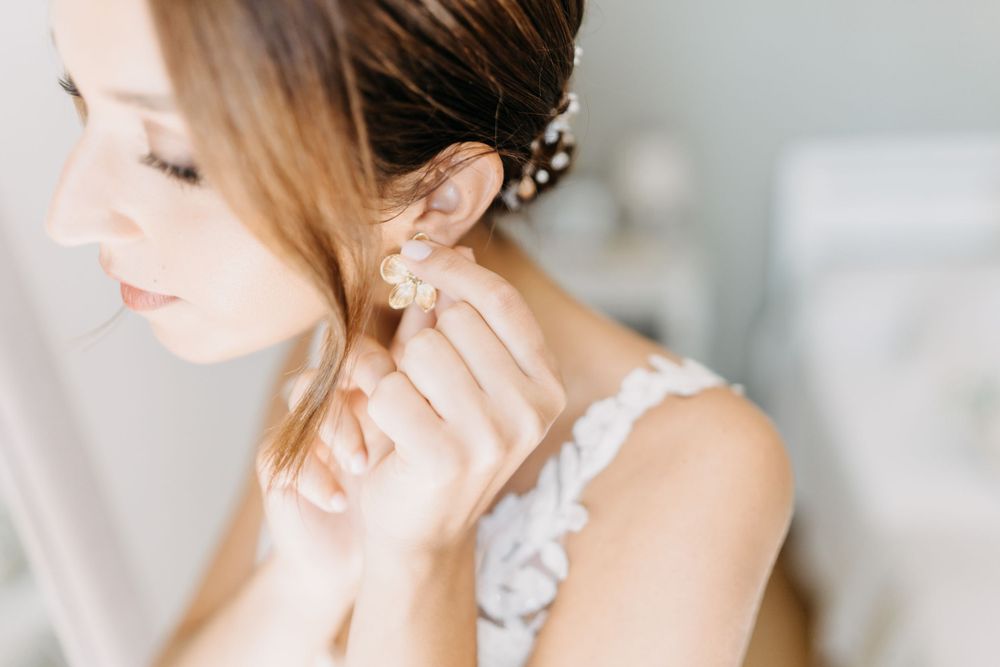 Close-up shot of someone putting on delicate pearl earrings while wearing an elegant white lace dress.