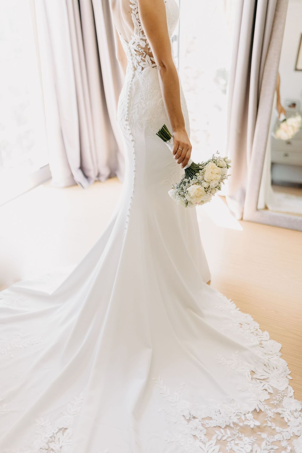 Elegant mermaid wedding dress with lace details and small bouquet.