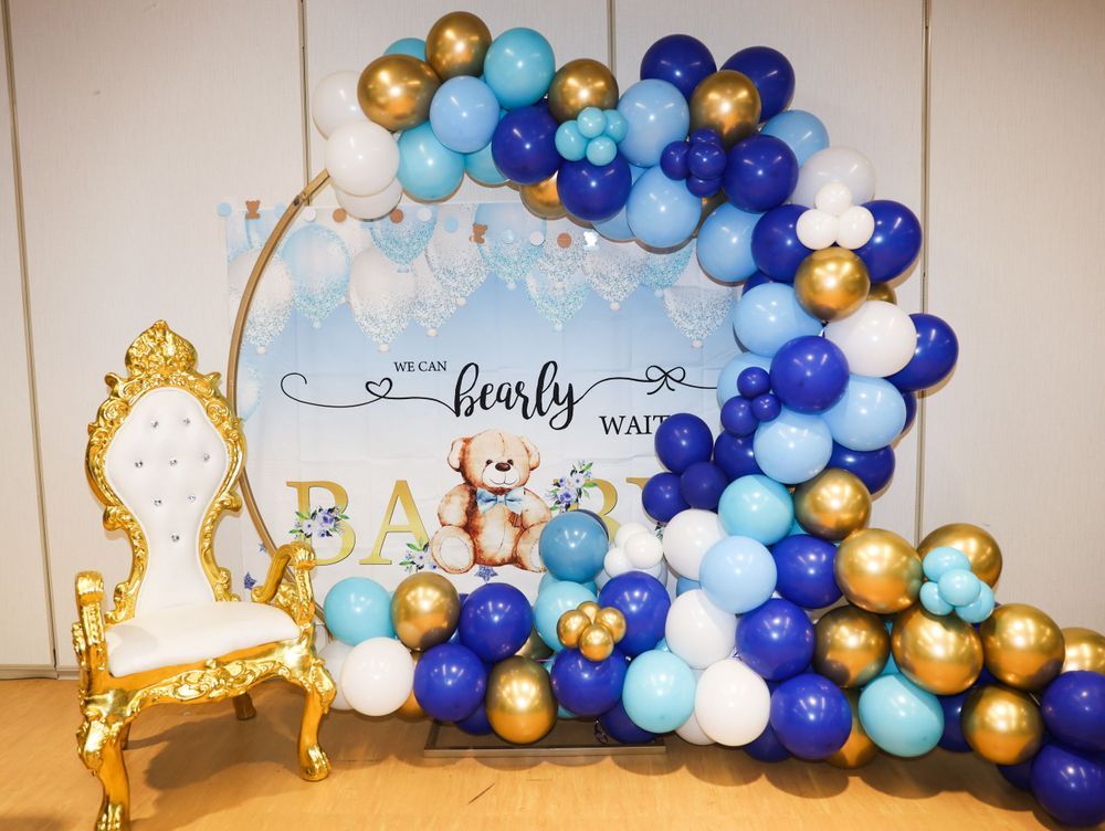 Baby shower decoration with blue and gold balloon arch and ornate gold throne chair.