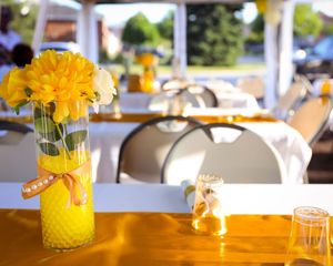 Yellow flowers in a vase with ribbon on outdoor table setting.