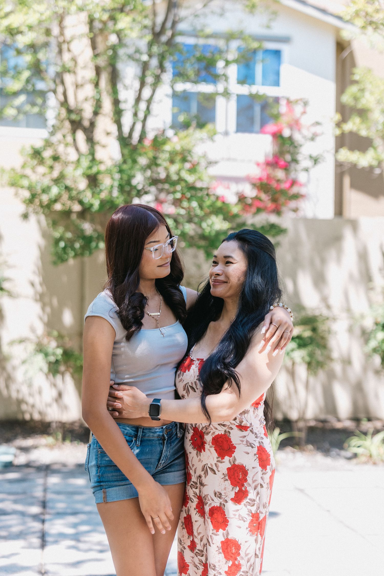 Friends share a joyful moment together outdoors in front of flowering bushes and a white wall.