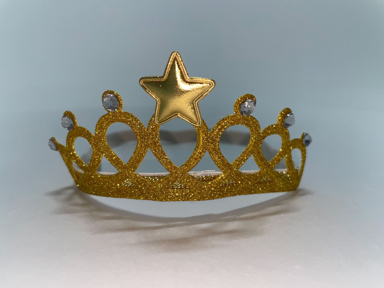Gold glitter princess crown with star detail photographed against blue background.