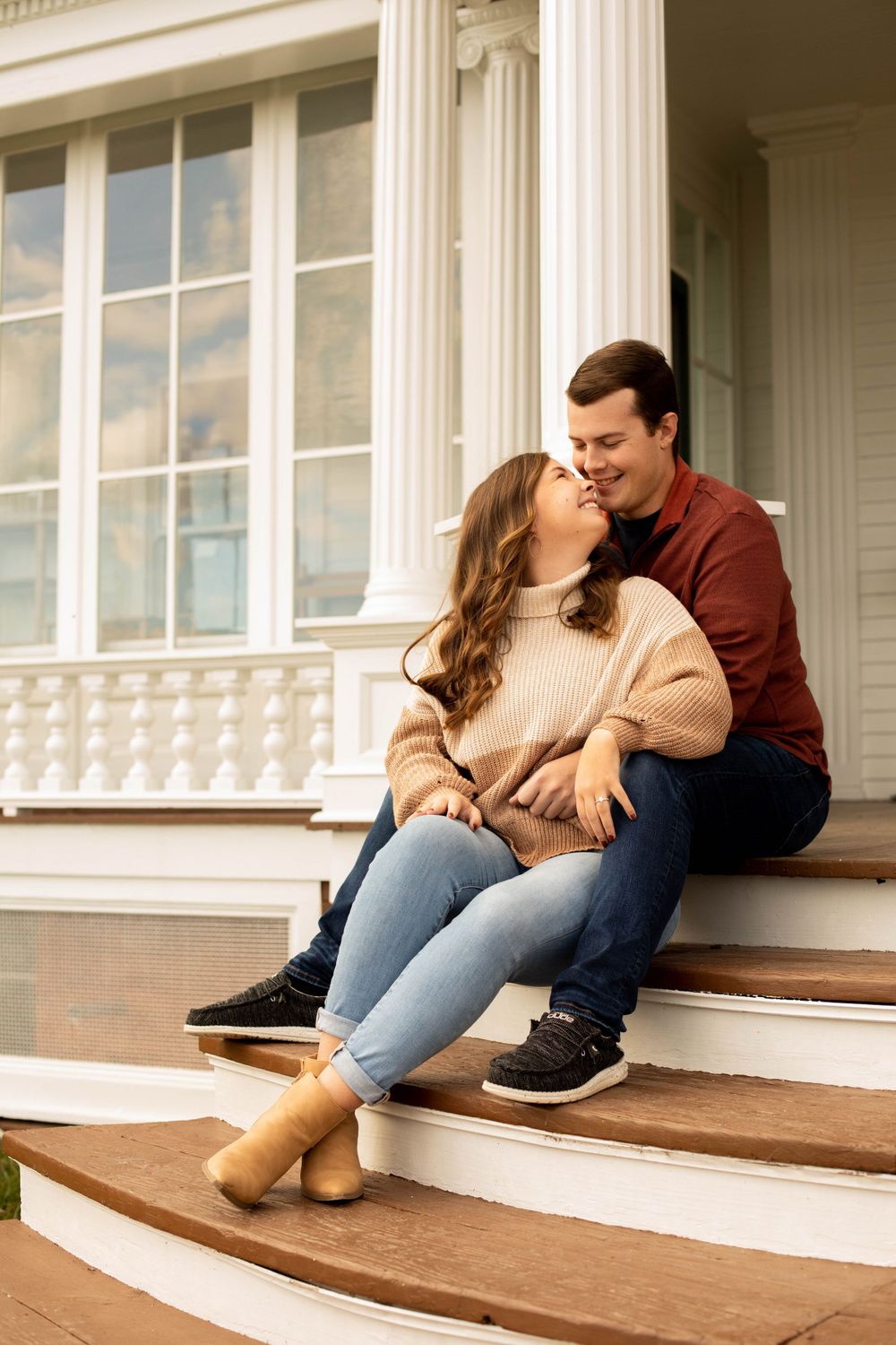 Couple relaxing on wooden porch steps in casual autumn attire.