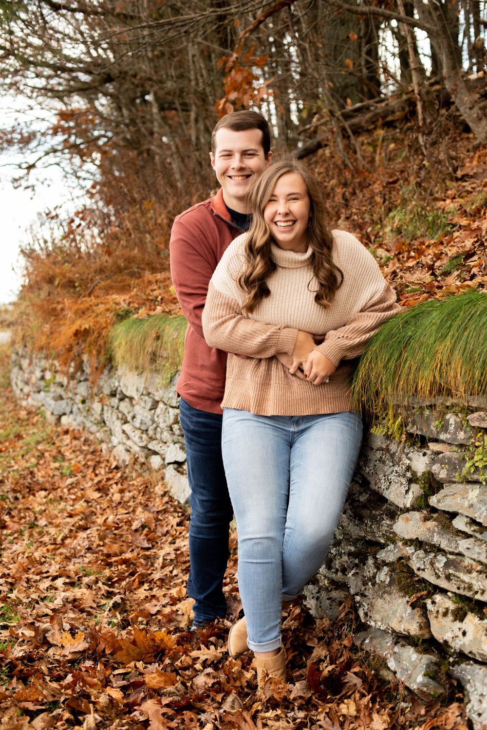 Couple embracing by stone wall surrounded by fall foliage.